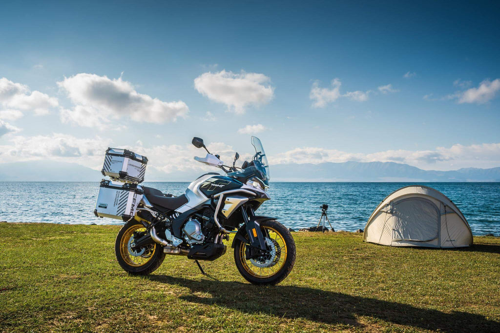 CFMOTO Mauritius 700MT motorcycle parked beside a tent near the water, ready for adventure.