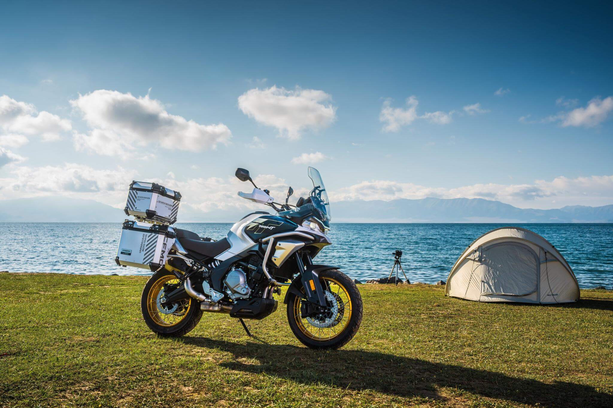 CFMOTO Mauritius 700MT motorcycle parked beside a tent near the water, ready for adventure.